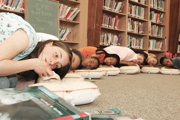 Kids practicing CPR on training kit in a library setting image