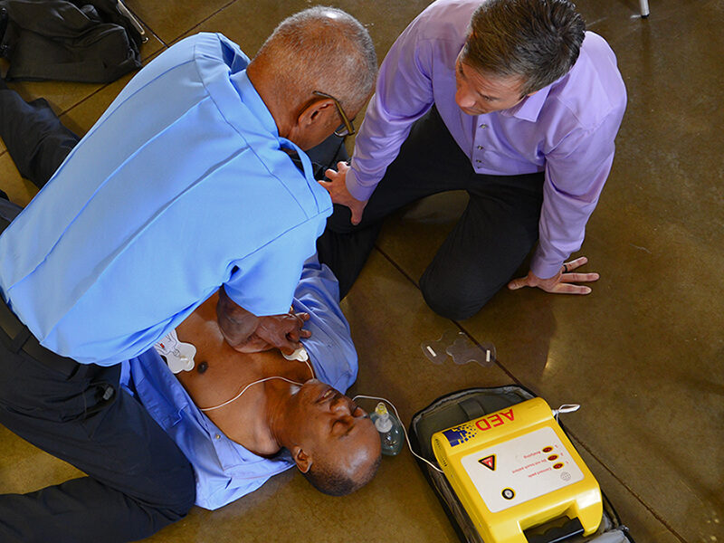 two men performing CPR with AED on unconscious man on the floor