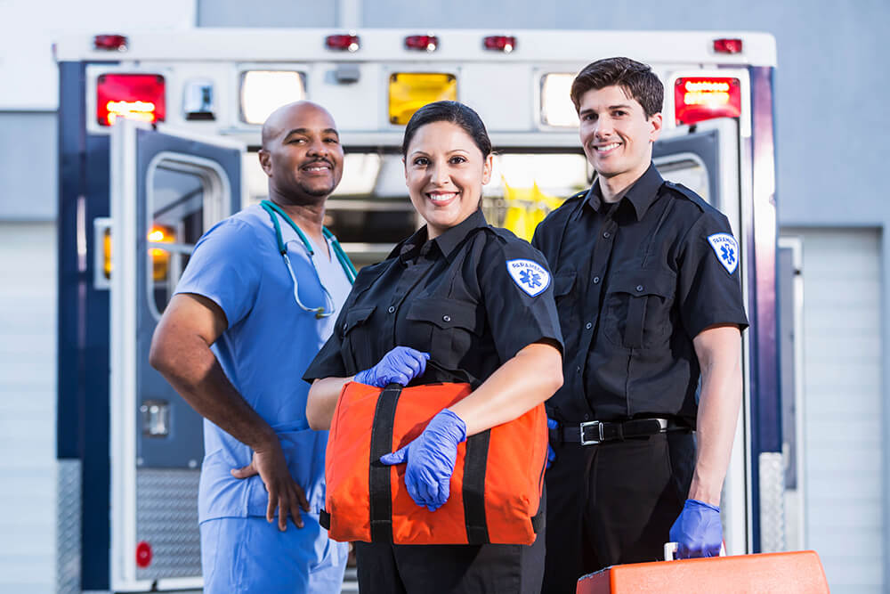 EMTs paramedics smiling in front of ambulance