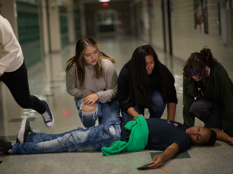 students kneeling over a fallen student