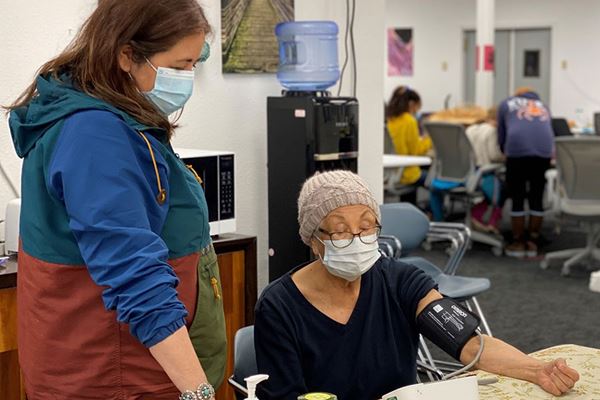 Woman helping elderly lady check her blood pressure at a community center