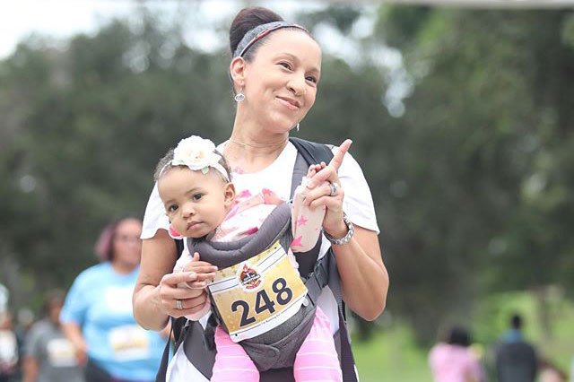 Woman with baby girl in chest carrier walking, participating in City of Champions 5k in Inglewood, CA