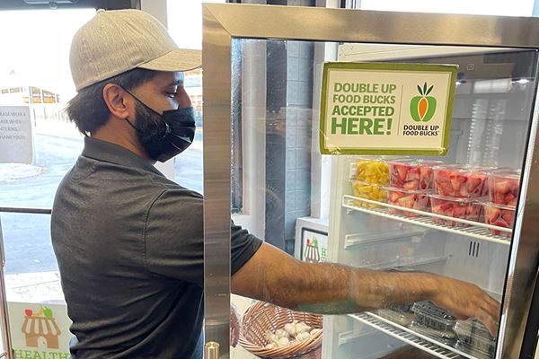 Man reaching into refrigerated shelves of fruit at corner store