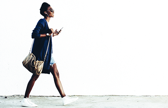 Athletic woman walking and listening to music via earbuds