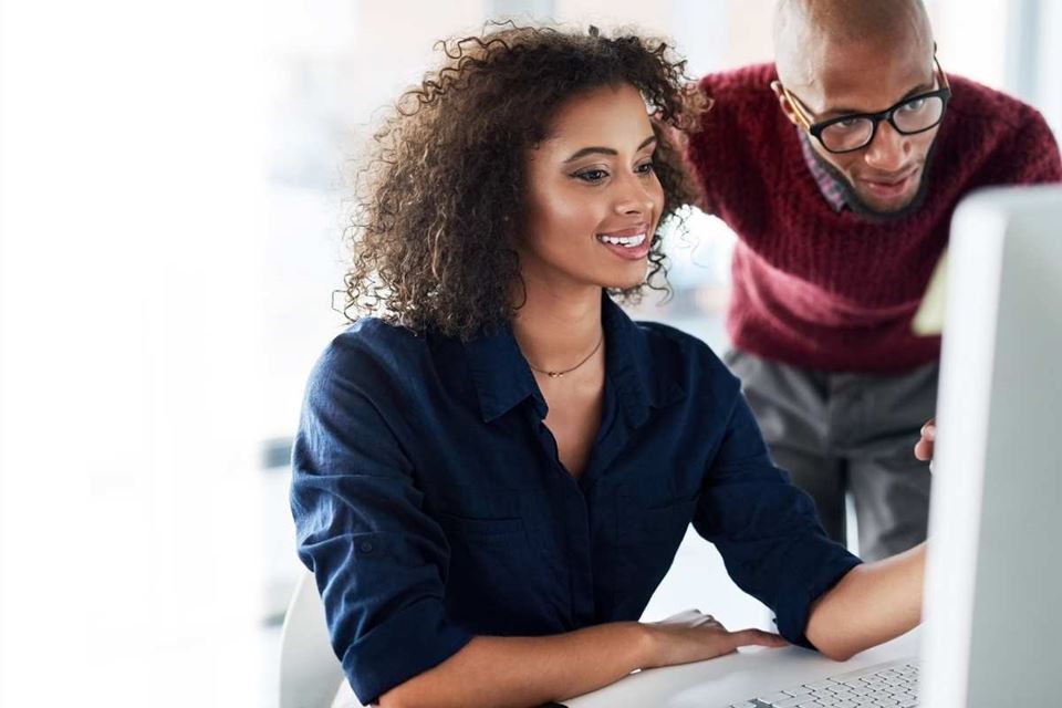 woman seated in front of computer with man leaning over