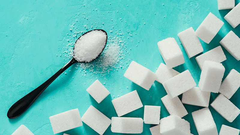 Sugar cubes and sugar in spoon. White sugar on turquoise background