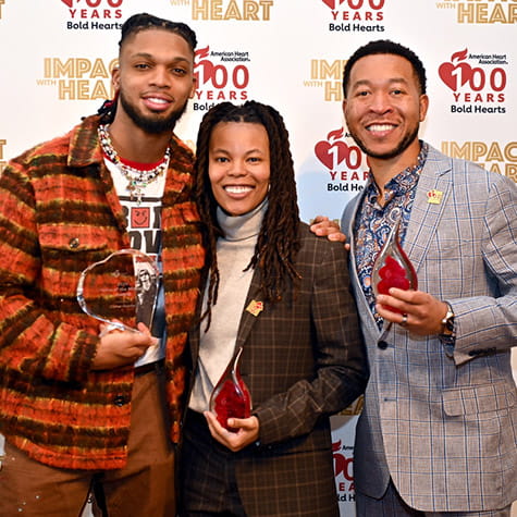 From left to right: Damar Hamlin, Ashley Williams and Andrew Suggs holding their Impact With Heart awards in front of a step and repeat background.
