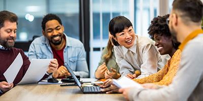 Employees in conference room around a laptop, smiling and talking together