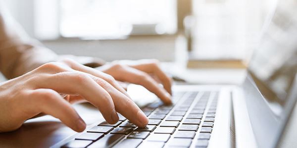 Close-up of hands typing on a laptop keyboard in a sunny room