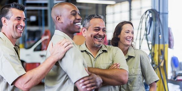 Group of smiling workers pose together in an automotive shop