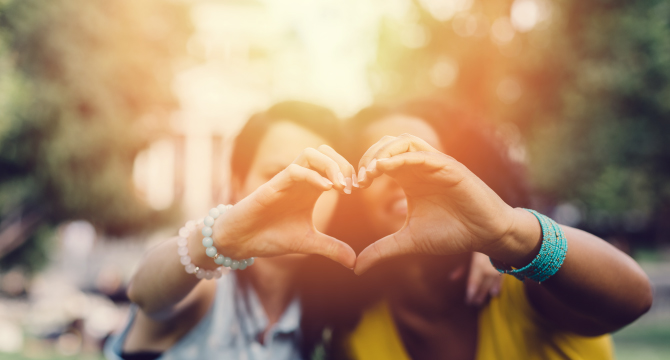 two women making a heart with hands